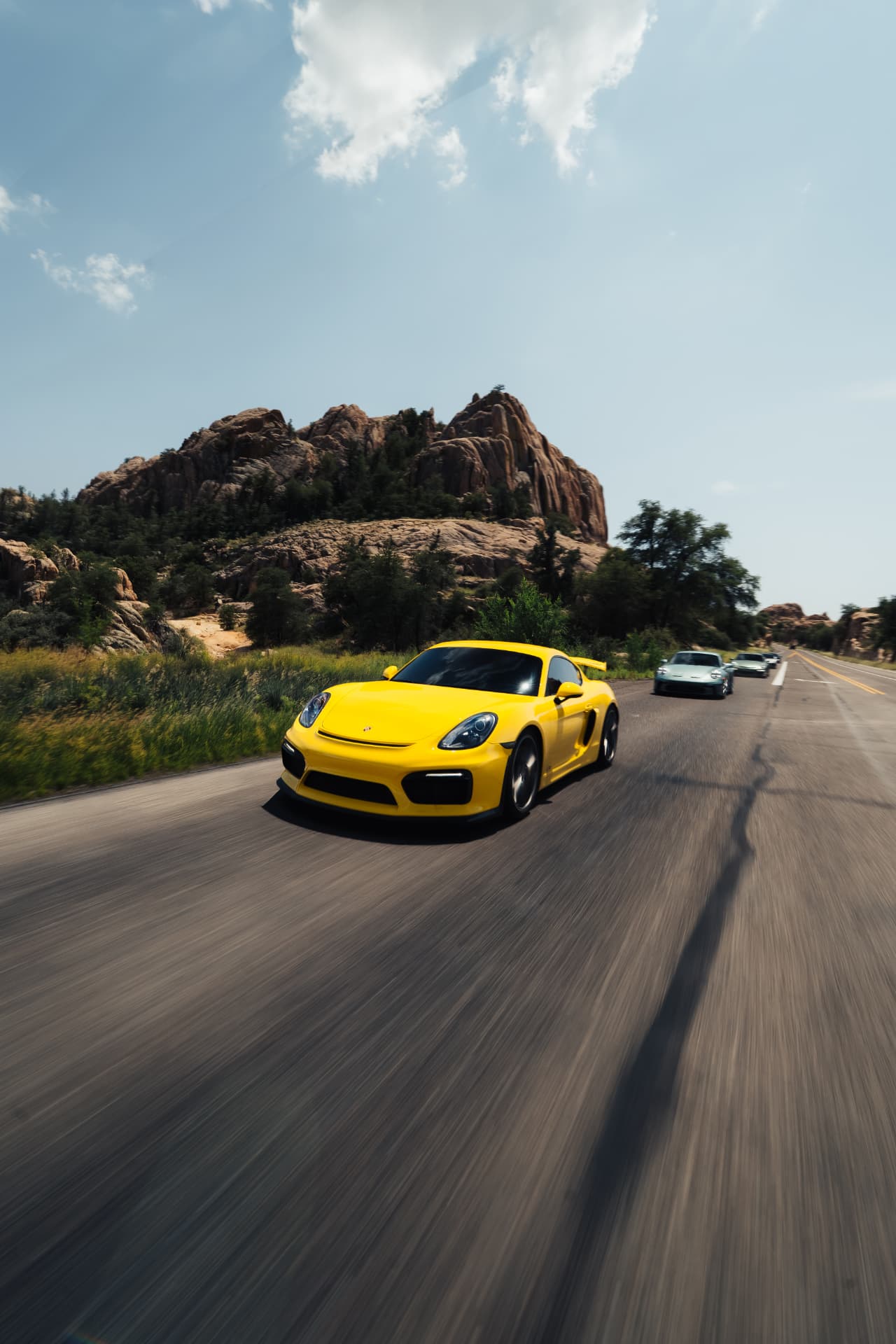 Yellow Porsche Cayman GT4 at speed past granite outcroppings