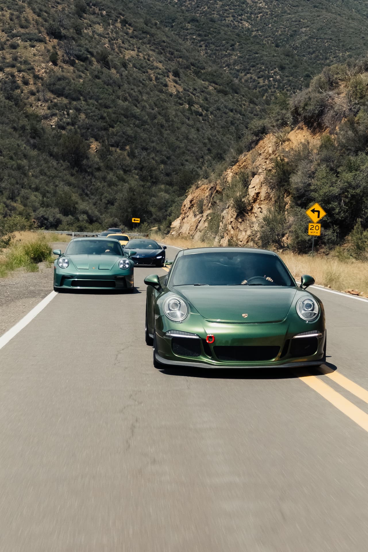 Two green Porsche 911s on a 20 mph canyon switchback
